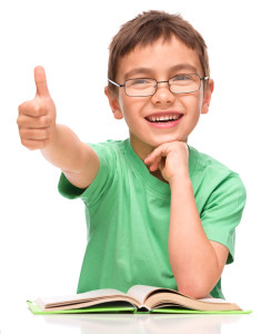 Cute little girl is reading a book and showing thumb up sign, is